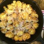 Crispy Smashed Potatoes topped with melted cheese in a black cast iron skillet on a striped kitchen towel
