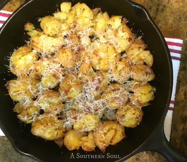 Crispy Smashed Potatoes topped with melted cheese in a black cast iron skillet on a striped kitchen towel