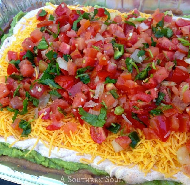 Layered Mexican Dip with Pico de Gallo in clear glass dish with guacamole, sour cream, cheese, and fresh tomato salsa garnish