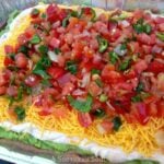 Layered Mexican Dip with Pico de Gallo topped with fresh tomatoes, cilantro, and cheese in a glass baking dish, overhead view