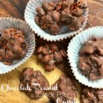 Chocolate Peanut Crock Pot Candy clusters with orange and black sprinkles in white paper cups on wood, Pinterest pin