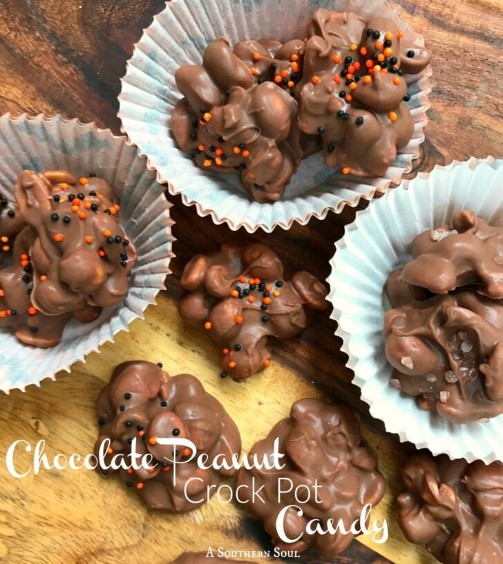 Chocolate Peanut Crock Pot Candy clusters with orange and black sprinkles in white paper cups on wood, Pinterest pin