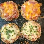 Four English Muffin Pizzas on dark griddle topped with melted cheese, ham, and green onions, two varieties shown