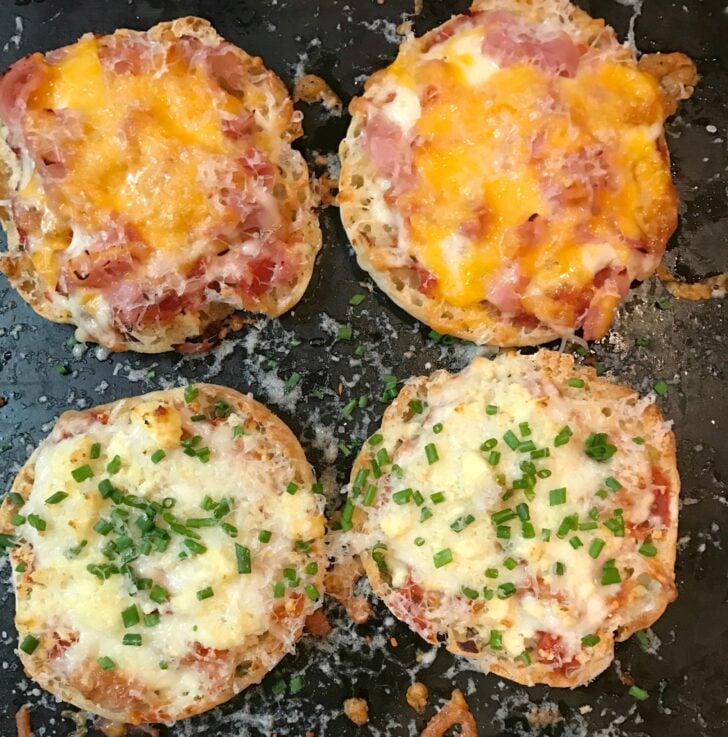 Four English Muffin Pizzas on dark griddle topped with melted cheese, ham, and green onions, two varieties shown
