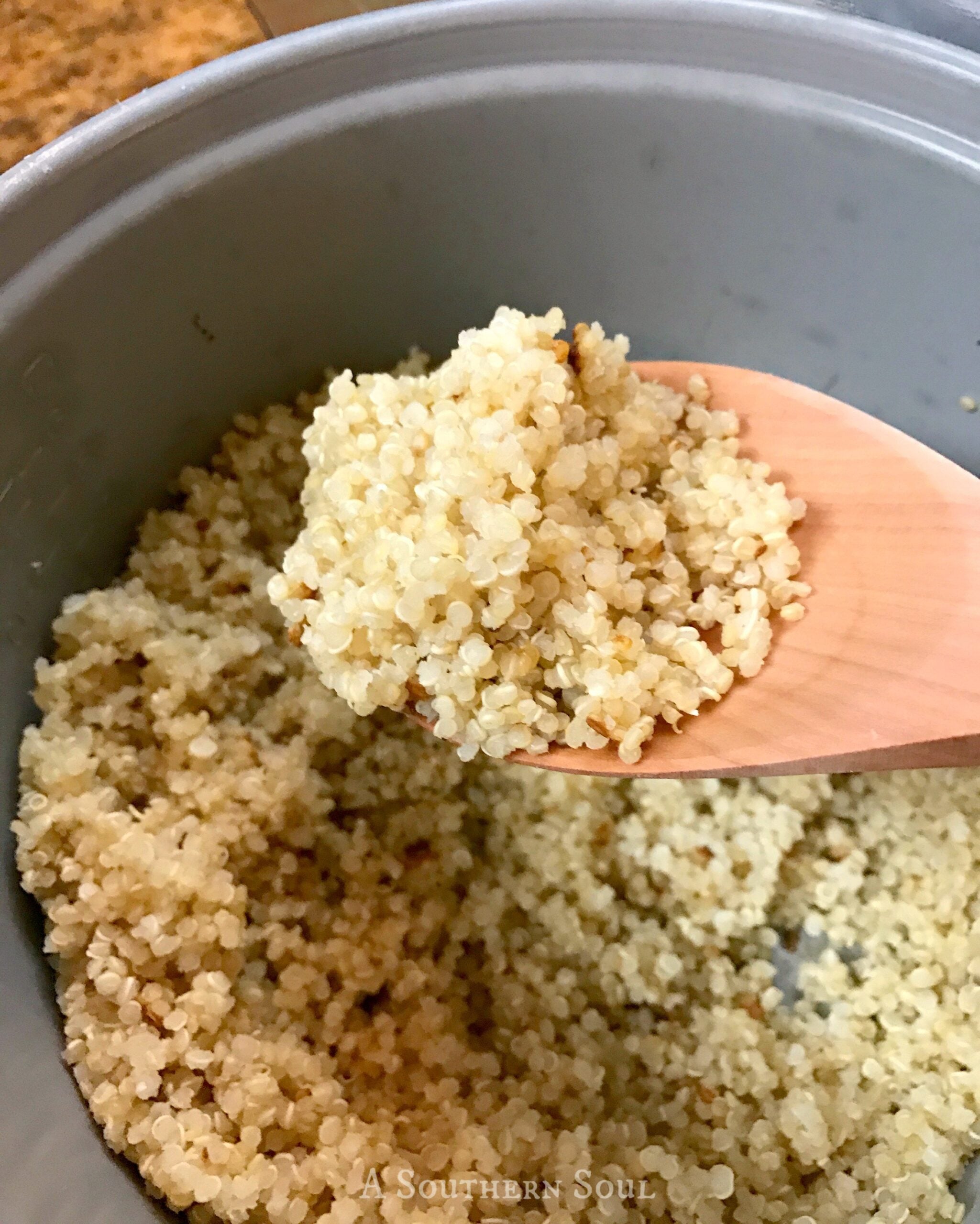 Fluffy quinoa being scooped from rice cooker with wooden spoon, showing cooked grains in pot