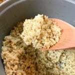 Fluffy quinoa in white rice cooker with wooden spoon holding cooked grains, Southern Soul recipe