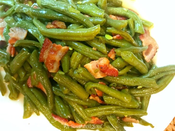 Southern Style Green Beans with bacon and seasonings served on a white plate, overhead shot with glossy green beans and crispy bacon pieces