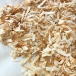 Shredded coconut flakes spread on white parchment paper showing How To Toast Coconut for Southern recipes