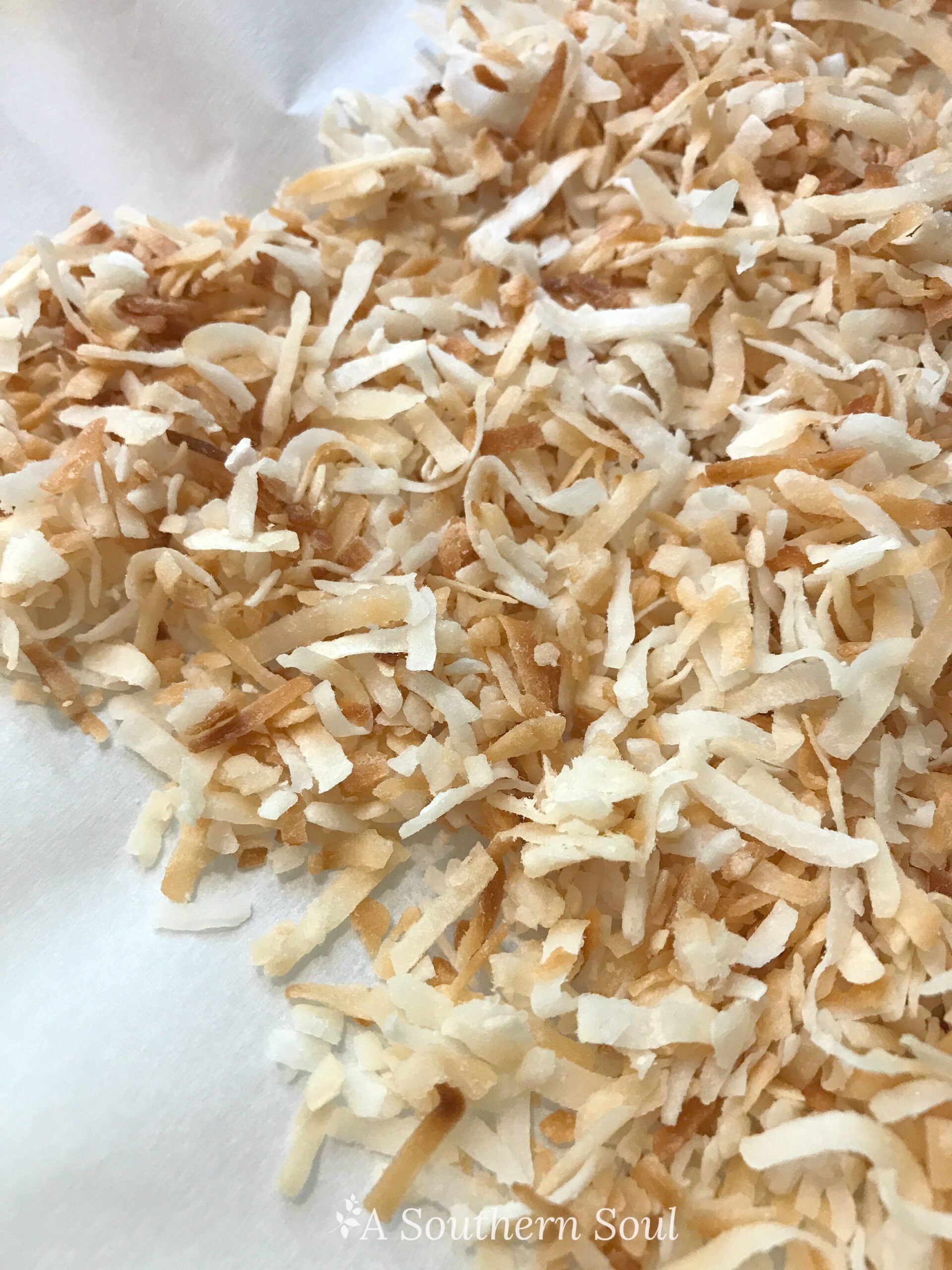 Shredded coconut flakes spread on white parchment paper showing How To Toast Coconut for Southern recipes