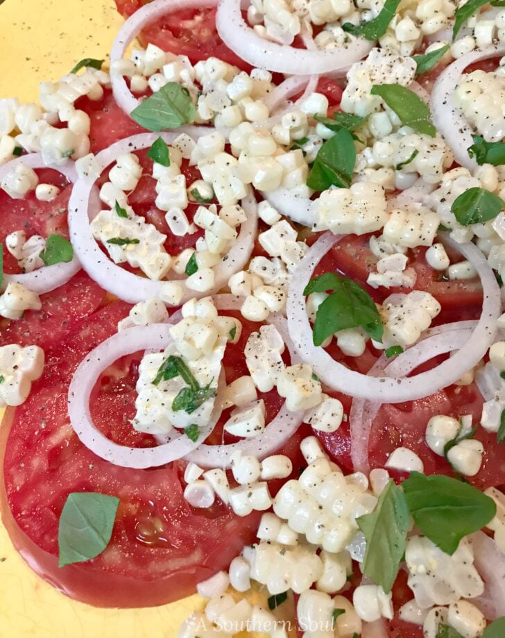 Tomato and corn summer salad with fresh mozzarella, red onion slices, basil, and black pepper on yellow background