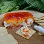 Pepper Jelly & Cream Cheese Appetizer on tan plate with crackers and knife, topped with red pepper jelly glaze