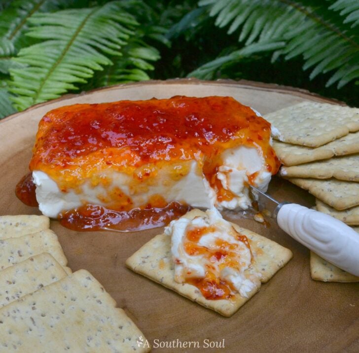 Pepper Jelly & Cream Cheese Appetizer on tan plate with crackers and knife, topped with red pepper jelly glaze