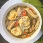 Chicken and Cheese Tortellini Soup in white bowl with pasta, shredded cheese, carrots, and beans in broth, overhead view