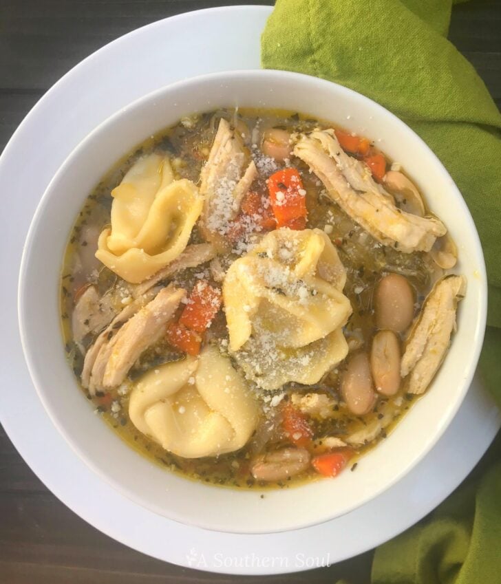 Chicken and Cheese Tortellini Soup in white bowl with pasta, shredded cheese, carrots, and beans in broth, overhead view