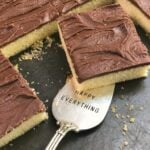 Vanilla Sheet Cake with Chocolate Fudge Icing sliced into squares with a silver spoon reading Happy Everything on dark surface