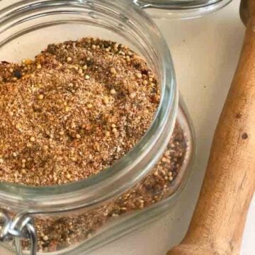 Homemade Montreal Steak Seasoning in glass jar with wooden spoon on white surface