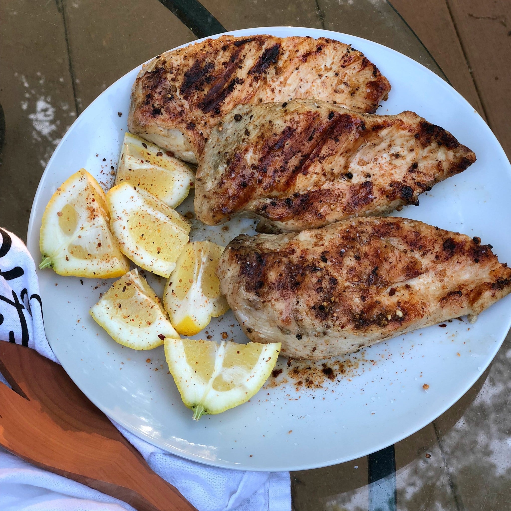 Grilled Lemon Pepper Chicken breasts with charred seasoning served on white plate with lemon wedges and black pepper