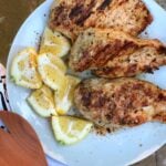 Grilled Lemon Pepper Chicken breasts on white plate with fresh lemon wedges and black pepper seasoning
