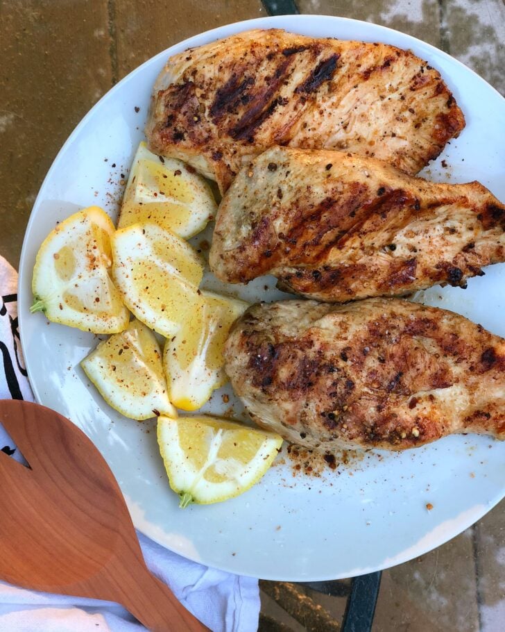 Grilled Lemon Pepper Chicken breasts on white plate with fresh lemon wedges and black pepper seasoning