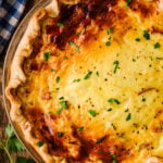 Golden Ham and Cheese Quiche in glass pie dish garnished with fresh parsley and black pepper on wooden surface