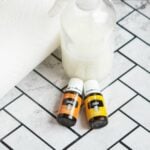 Homemade Streak Free Glass Cleaner with orange and lemon essential oil bottles next to spray bottle on marble tile
