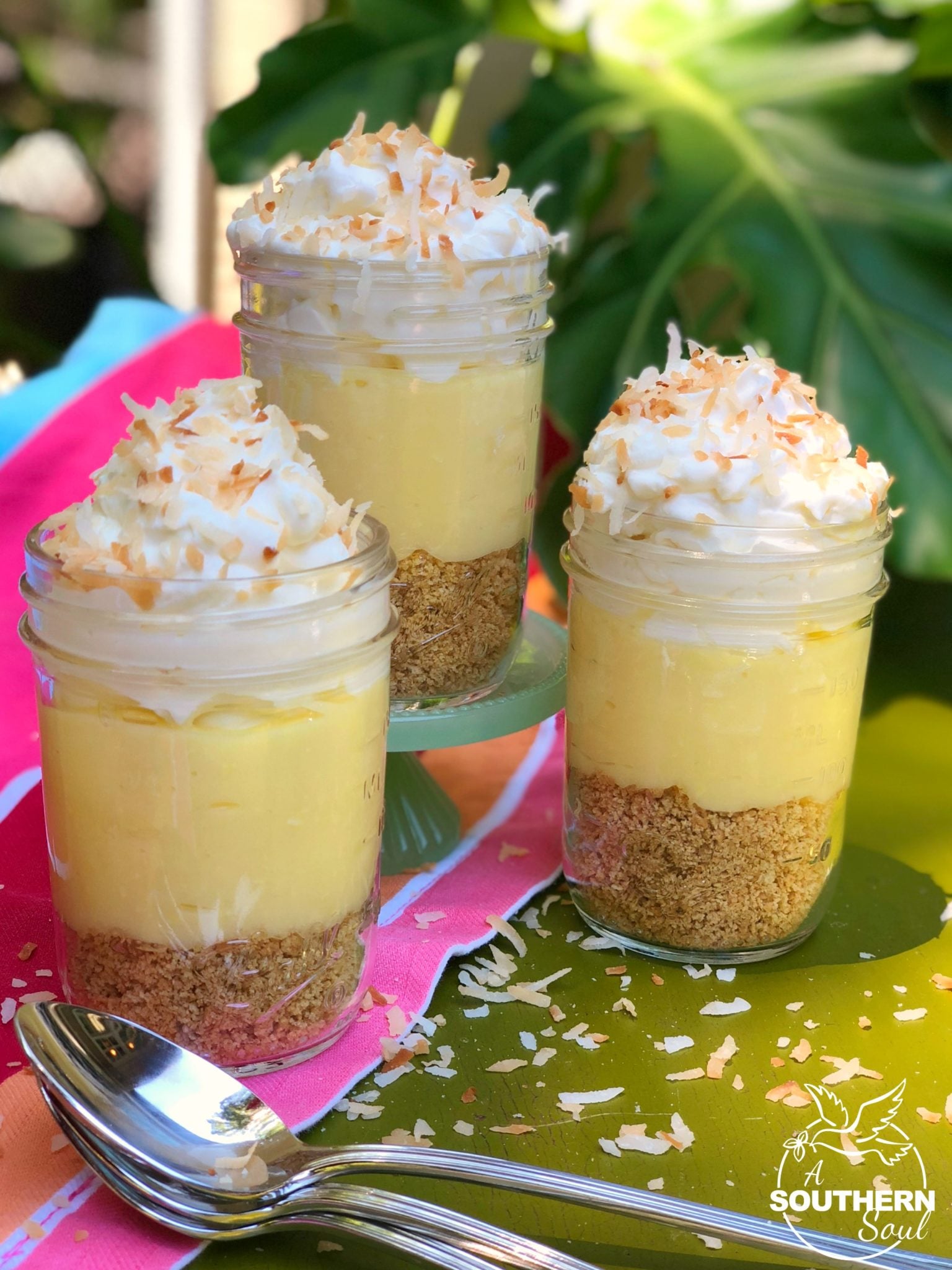Three No Bake Coconut Cream Pie In Jars with graham cracker crust, creamy filling, whipped topping and toasted coconut flakes in glass jars