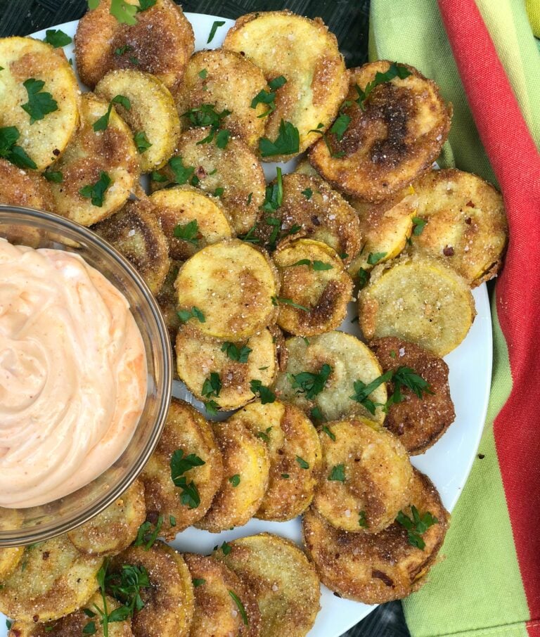 Southern Fried Squash rounds on white plate with creamy dipping sauce, fresh parsley garnish, and colorful napkins