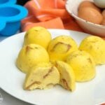 Instant Pot Bacon & Cheese Egg Bites on a white plate, golden-yellow with visible bacon pieces, beside brown eggs and blue baking cups