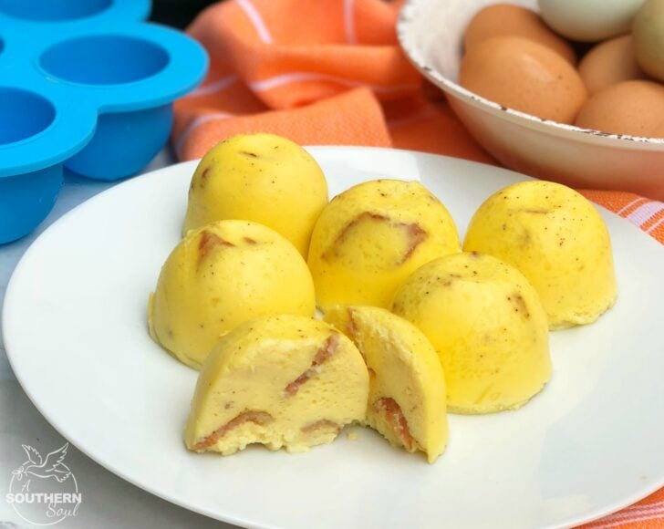 Instant Pot Bacon & Cheese Egg Bites on a white plate, golden-yellow with visible bacon pieces, beside brown eggs and blue baking cups