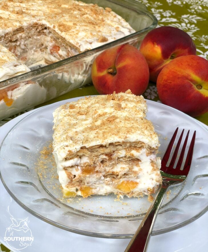 Slice of Peaches & Cream Icebox Cake on glass plate with fork, showing layers of wafers, whipped cream, and peaches; fresh peaches and full