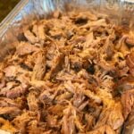 Simple Smoked Pulled Pork in aluminum pan, shredded and seasoned, overhead view with white plate nearby