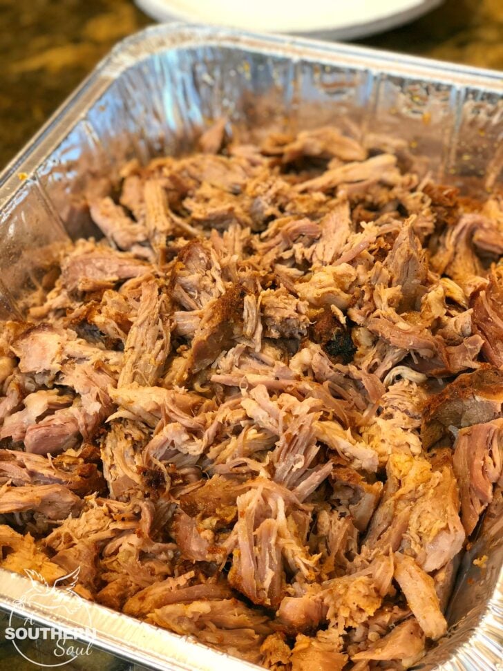 Simple Smoked Pulled Pork in aluminum pan, shredded and seasoned, overhead view with white plate nearby