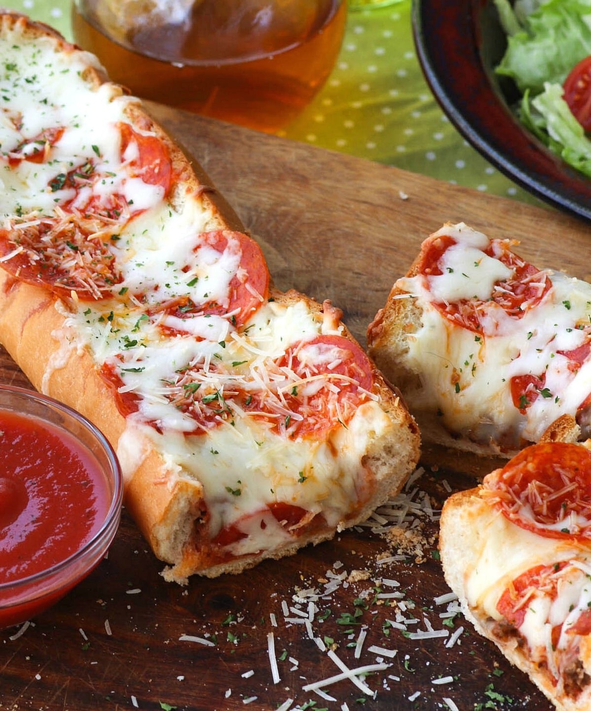 Meat Lovers Stuffed French Bread Pizza sliced on wood board with marinara sauce, salad, and beverage nearby