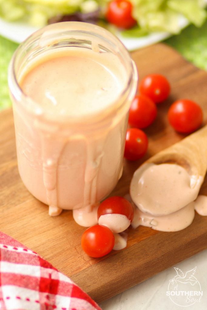 A closeup of this creamy, flavorful thousand island dressing shows it's pale peach color as it spills over the sides of the mason jar.