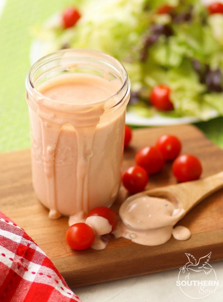 A wooden spoon has been dipped into this rich, flavorful, creamy Thousand Island Dressing, and then set to the side as the dressing spills over the sides of the mason jar it's in.