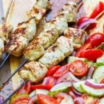 Grilled Chicken Souvlaki Skewers are juicy and tender. Make with lemon juice, oregano, garlic, salt and pepper. Add in a chopped salad with tomatoes, onions and cucumbers and you've got a meal your friends and family will love!