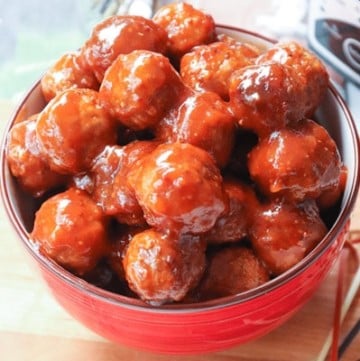 Game Day Crock Pot Meatballs in red bowl with glossy sauce coating, overhead view on light background