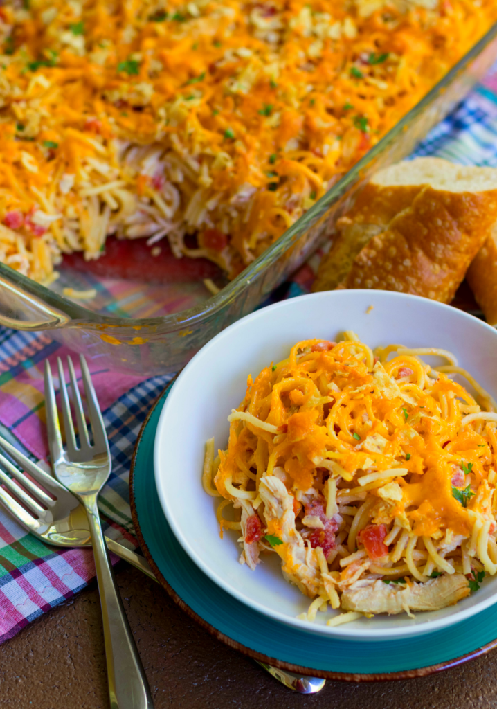 On a white plate next to warm bread, sits a single serving of Out of This World Rotel Chicken Spaghetti casserole.
