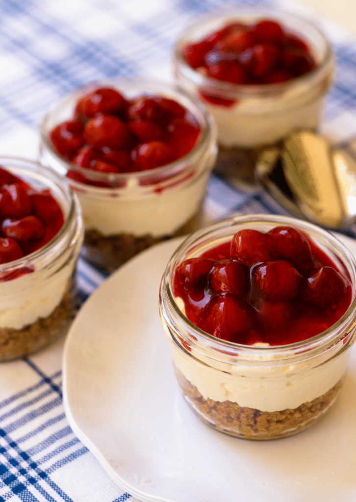 No Bake Cherry Delight In Jars is a yummy, easy to make dessert. A crust made with crushed graham crackers, butter and sugar is layered into small jars then topped with a mixture of cream cheese, powdered sugar and fresh whipped cream all topped with cherry pie filling.