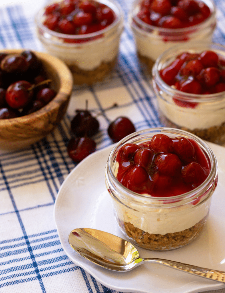 No Bake Cherry Delight In Jars is a yummy, easy to make dessert. A crust made with crushed graham crackers, butter and sugar is layered into small jars then topped with a mixture of cream cheese, powdered sugar and fresh whipped cream all topped with cherry pie filling.