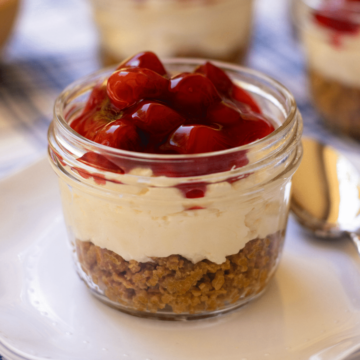 No Bake Cherry Delight In Jars is a yummy, easy to make dessert. A crust made with crushed graham crackers, butter and sugar is layered into small jars then topped with a mixture of cream cheese, powdered sugar and fresh whipped cream all topped with cherry pie filling.