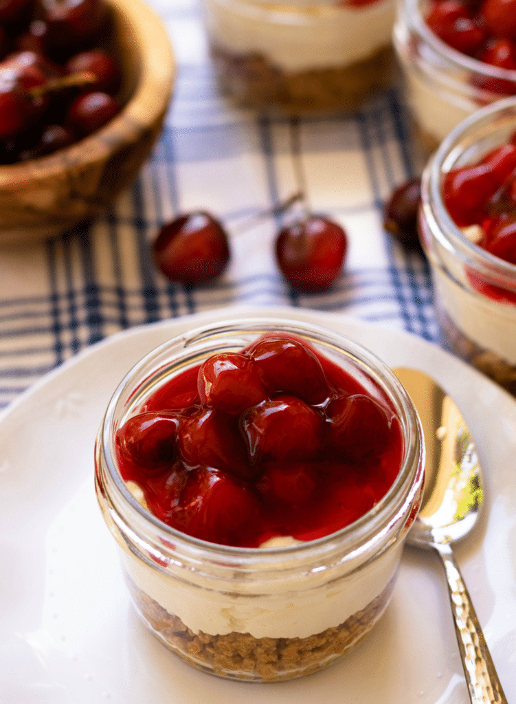 No Bake Cherry Delight In Jars is a yummy, easy to make dessert. A crust made with crushed graham crackers, butter and sugar is layered into small jars then topped with a mixture of cream cheese, powdered sugar and fresh whipped cream all topped with cherry pie filling.