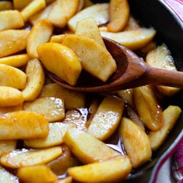 Cinnamon Apples cooked in a cast iron skillet using a wooden spoon.
