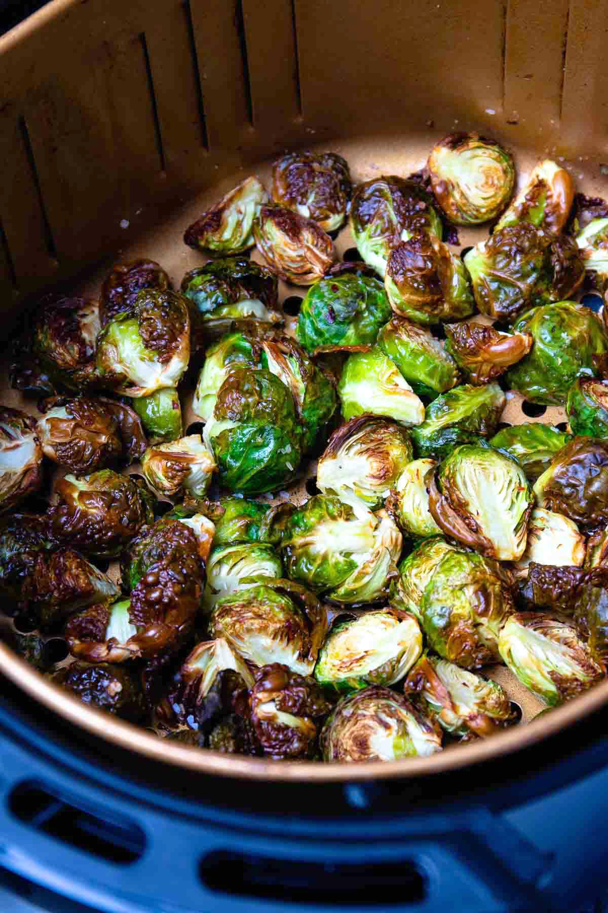 Perfectly cooked brussel sprouts in the basket of an air fryer.