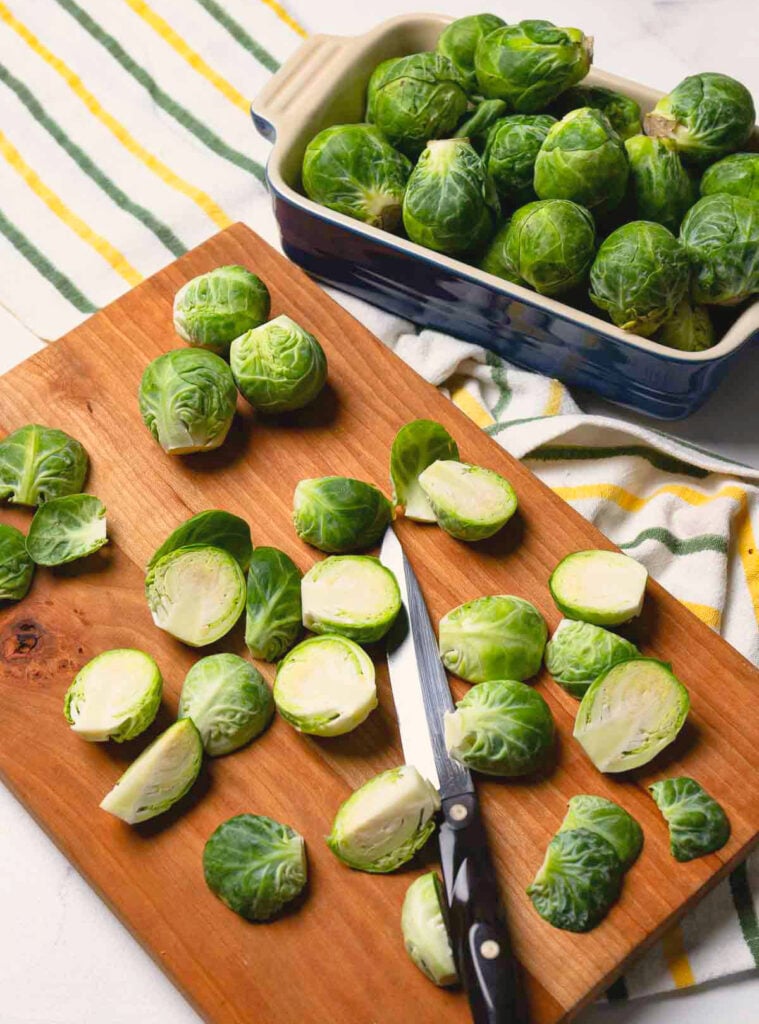 Raw brussel sproutson a cutting board with a knife to be cooked in an air fryer.