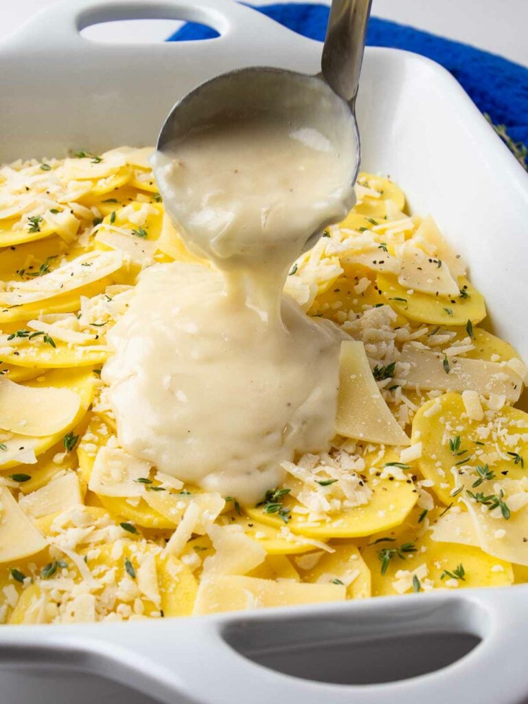 Scalloped Potatoes with Parmesan cheese and thyme in baking dish with sauce pour over.