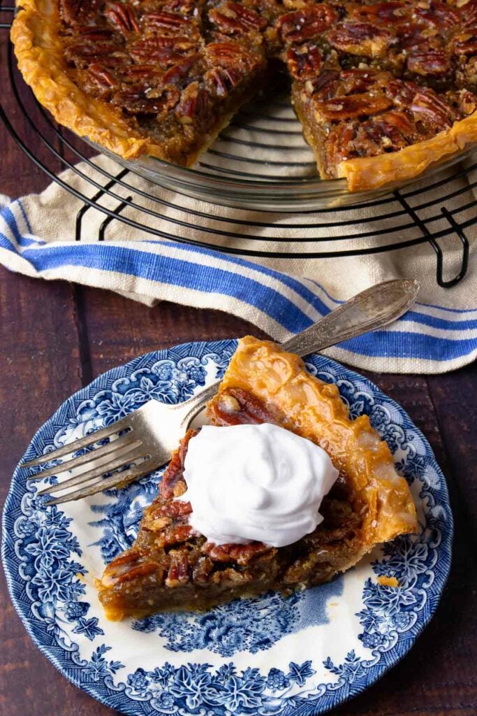 Maple Bourbon Pecan Pie slice with whipped cream on a blue plate with fork.