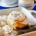 Easy to make Cinnamon Rolls in a pan being scooped with a copper utensil served with a cup of coffee.