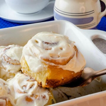 Easy to make Cinnamon Rolls in a pan being scooped with a copper utensil served with a cup of coffee.