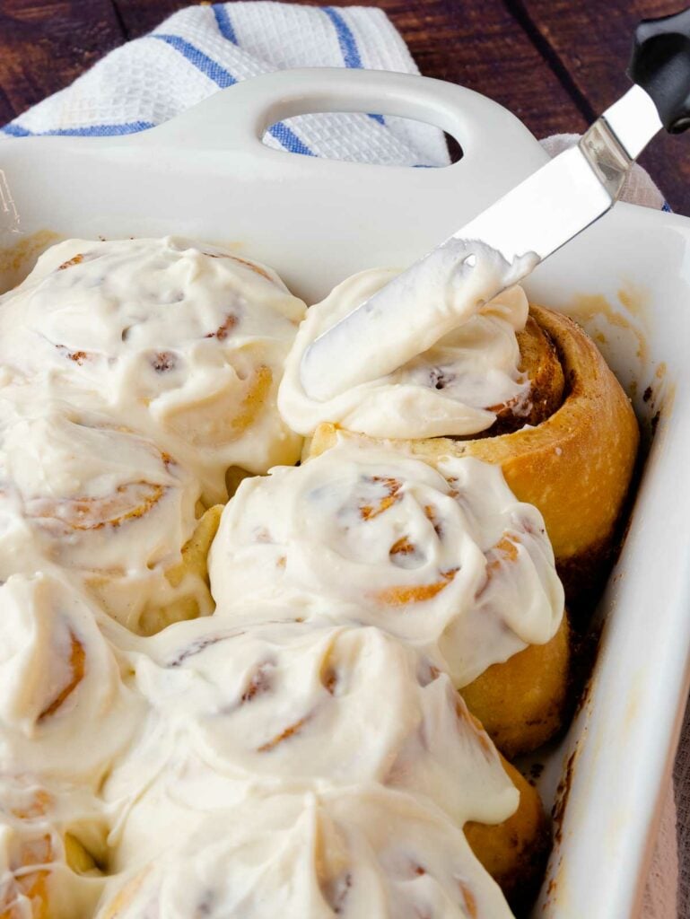 Easy Cinnamon Rolls in a white pan with a knife icing the rolls.